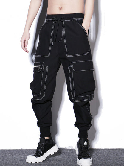 Person wearing black cargo pants with white stitching on a white background