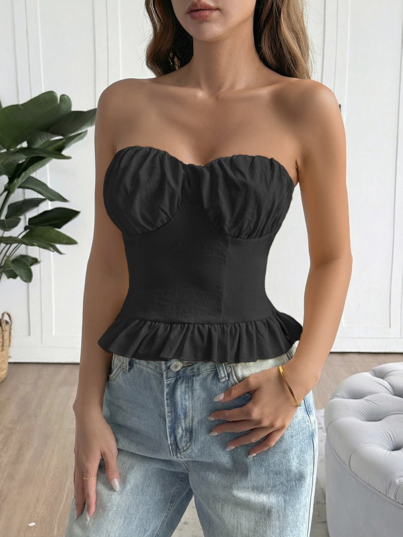 Woman wearing a black strapless top with ruffled details and light blue jeans indoors.