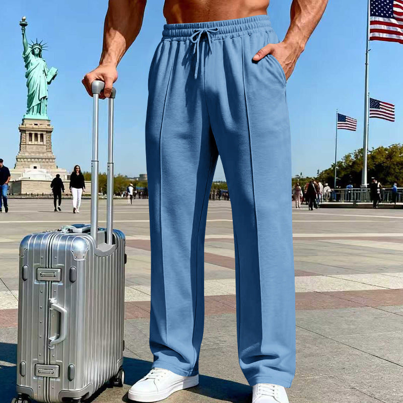 Person wearing blue pants standing next to a silver suitcase with the Statue of Liberty and American flags in the background.