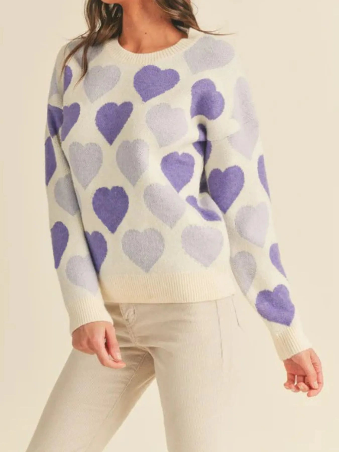 Person wearing a sweater with purple heart pattern on a beige background
