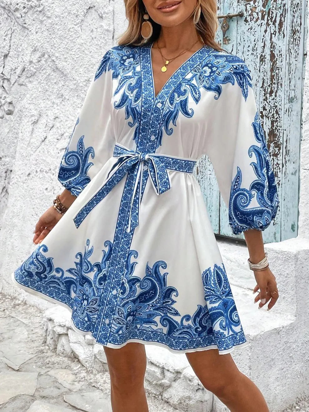 White dress with blue floral patterns worn by a person against a textured white wall.