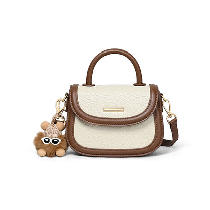 White handbag with brown accents and a teddy bear charm on a white background