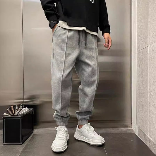 Person wearing a black sweatshirt, gray jogger pants, and white sneakers in an indoor setting.