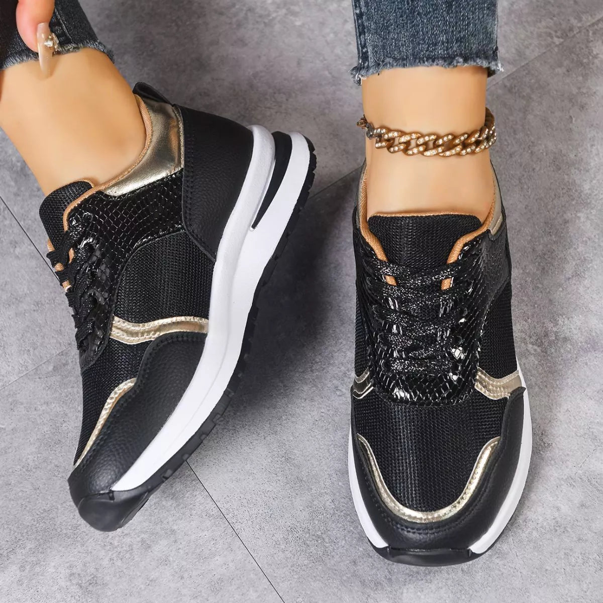 Black and gold sneakers worn with jeans on a gray floor.