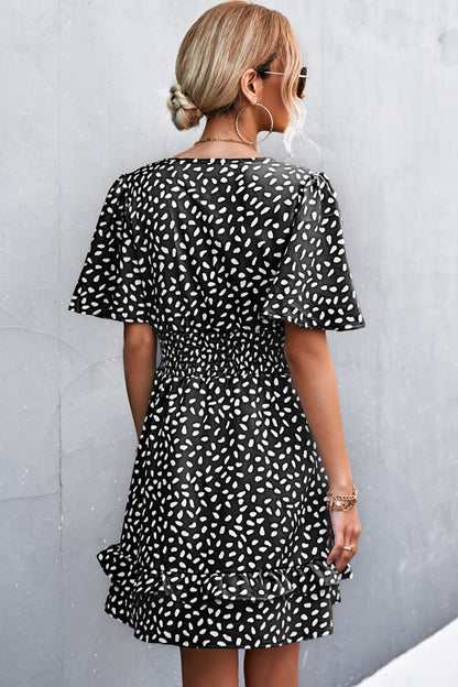 Woman wearing a black and white patterned dress against a gray wall.