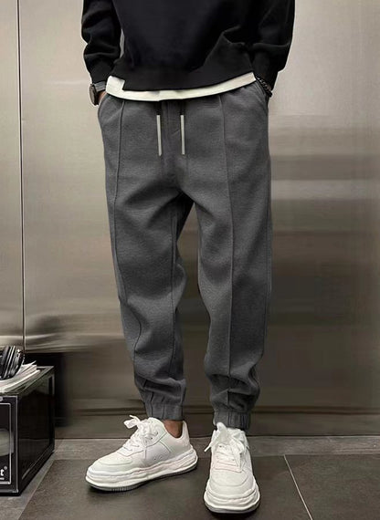 Person wearing dark sweatshirt, gray jogger pants, and white sneakers against a neutral background