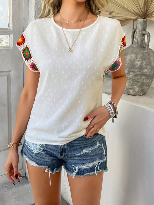 Woman wearing a white polka dot shirt with colorful sleeves and denim shorts indoors.