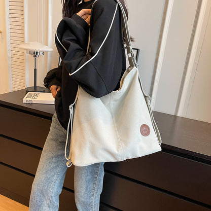 Person holding a white tote bag with a brand logo in a room setting.