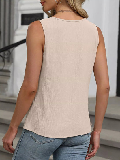 Woman wearing a beige sleeveless top and blue jeans standing outdoors.