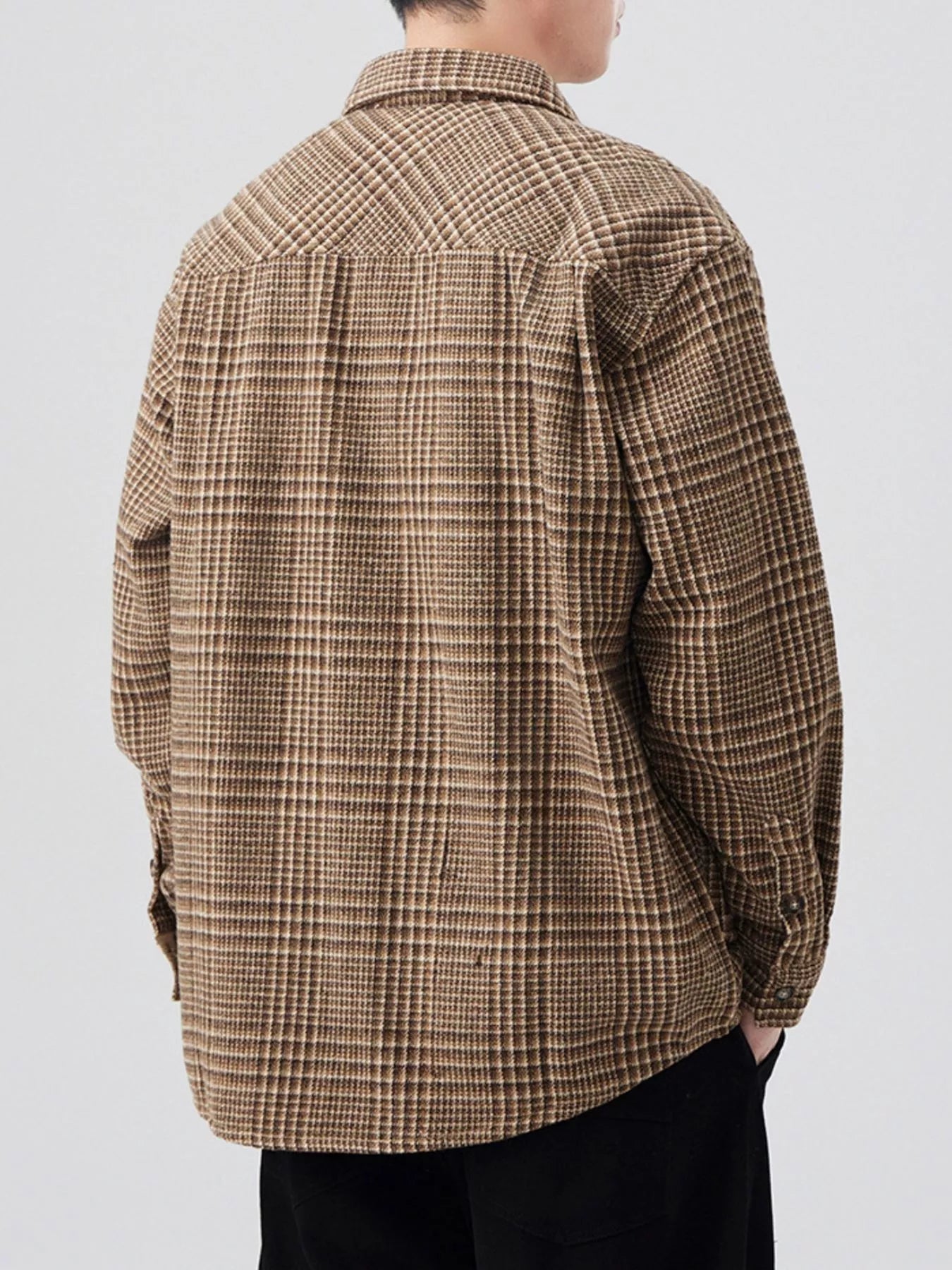 Person wearing a brown checkered shirt on a light gray background
