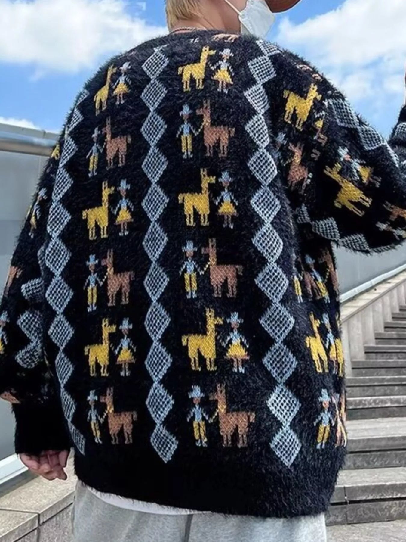 Person wearing a dark sweater with colorful llama pattern outdoors.