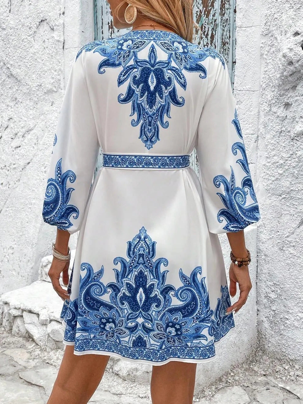 White dress with blue intricate patterns worn by a person against a textured wall.
