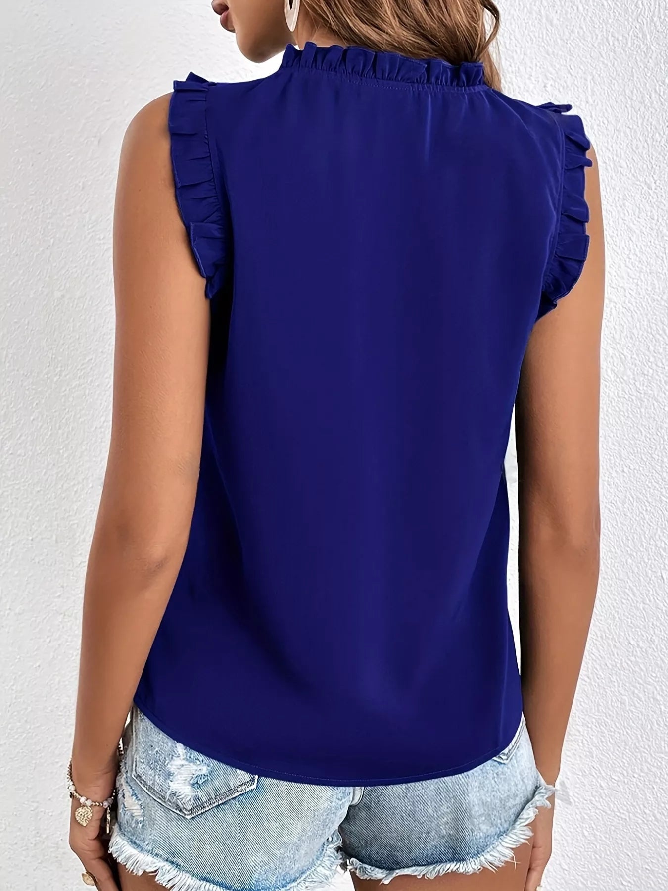 Person wearing a blue sleeveless top with ruffled shoulders against a white background