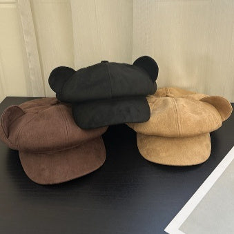 Three hats in black, brown, and beige on a dark surface with a light background