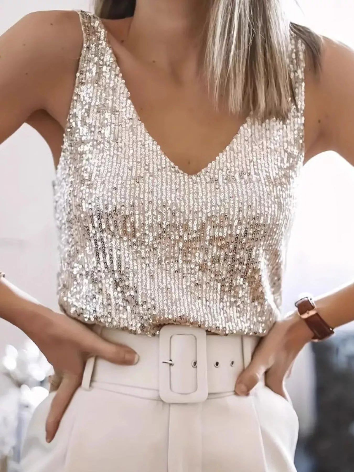 Person wearing a sparkly top and white pants with a blurred background