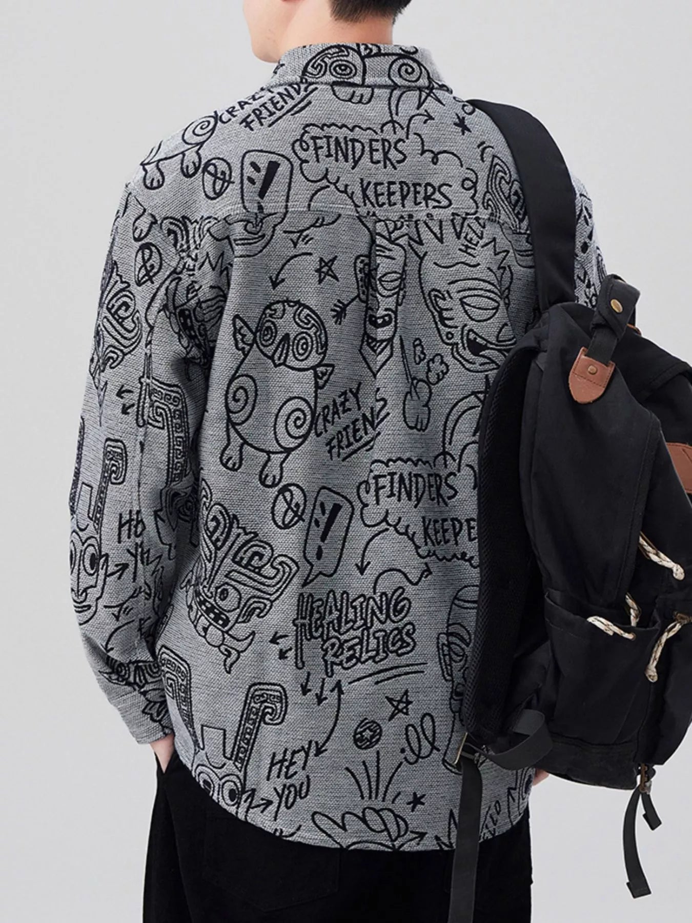 Person wearing a gray shirt with black graphic designs, standing against a white background.