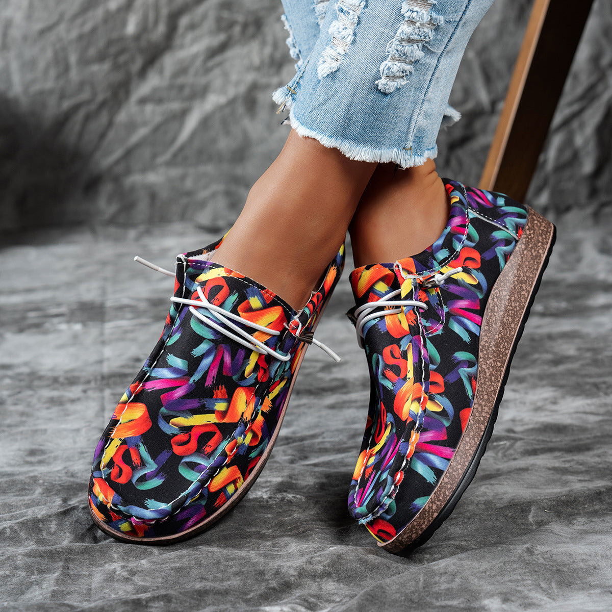 Colorful patterned shoes worn with denim jeans on a gray surface