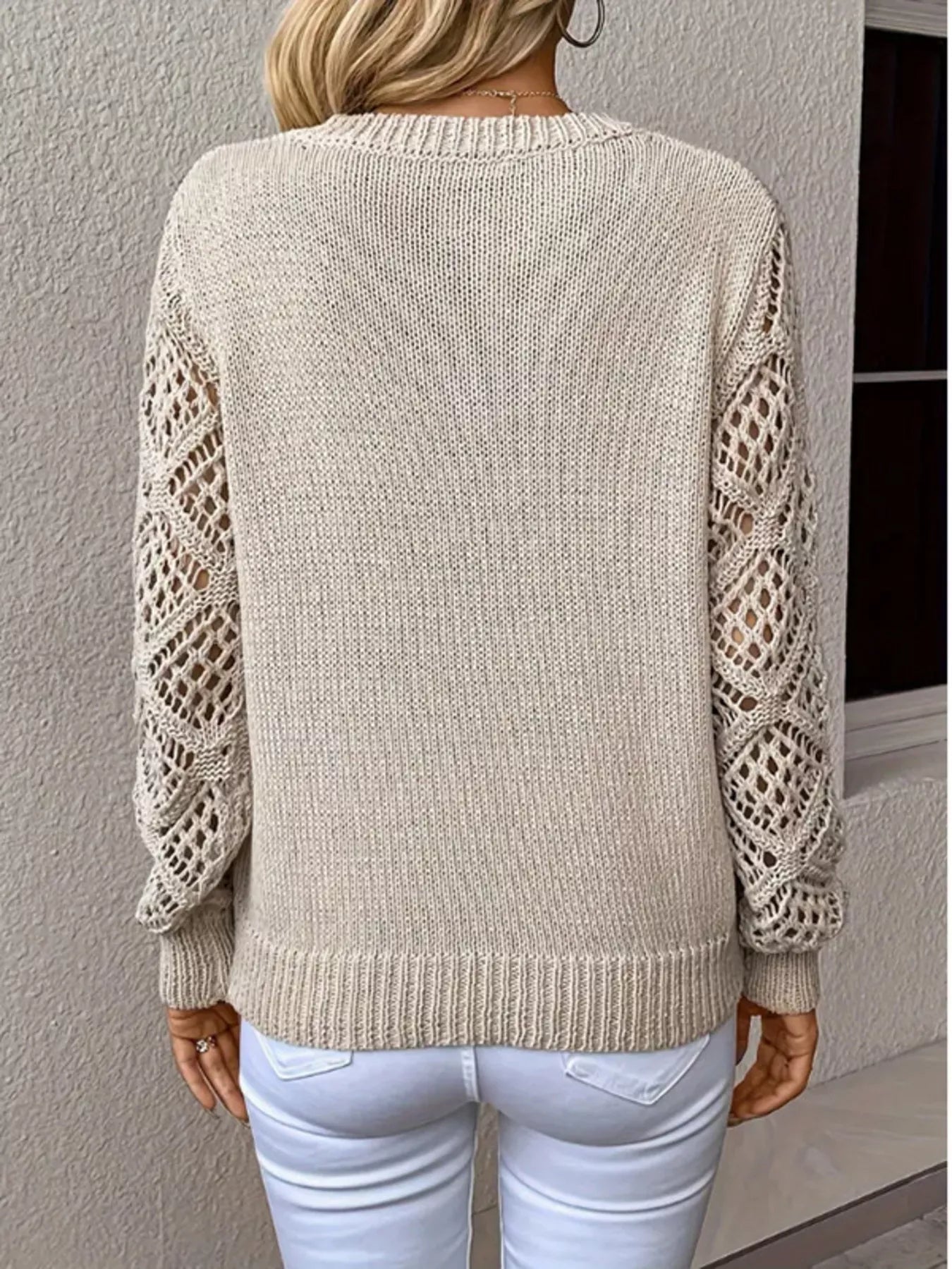 Beige sweater with open knitted sleeves worn by a person against a neutral background