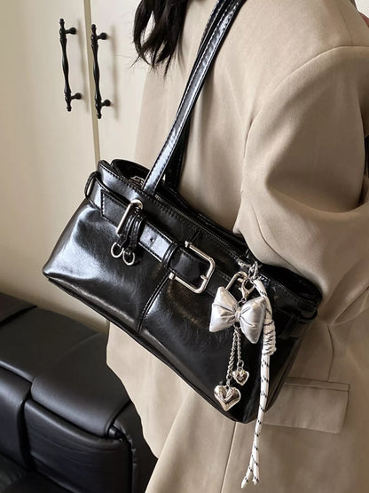 Black handbag with decorative charms held by a person wearing a beige coat.