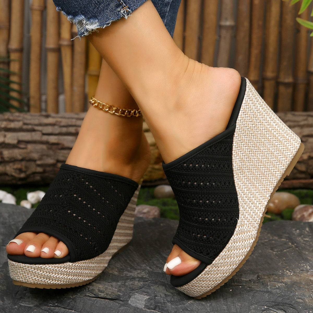 Black wedge sandals with woven design on a stone surface