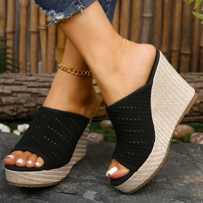 Black wedge sandals with woven design on a stone surface