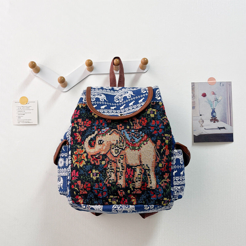 Decorative backpack with elephant design hanging on a wall hook.