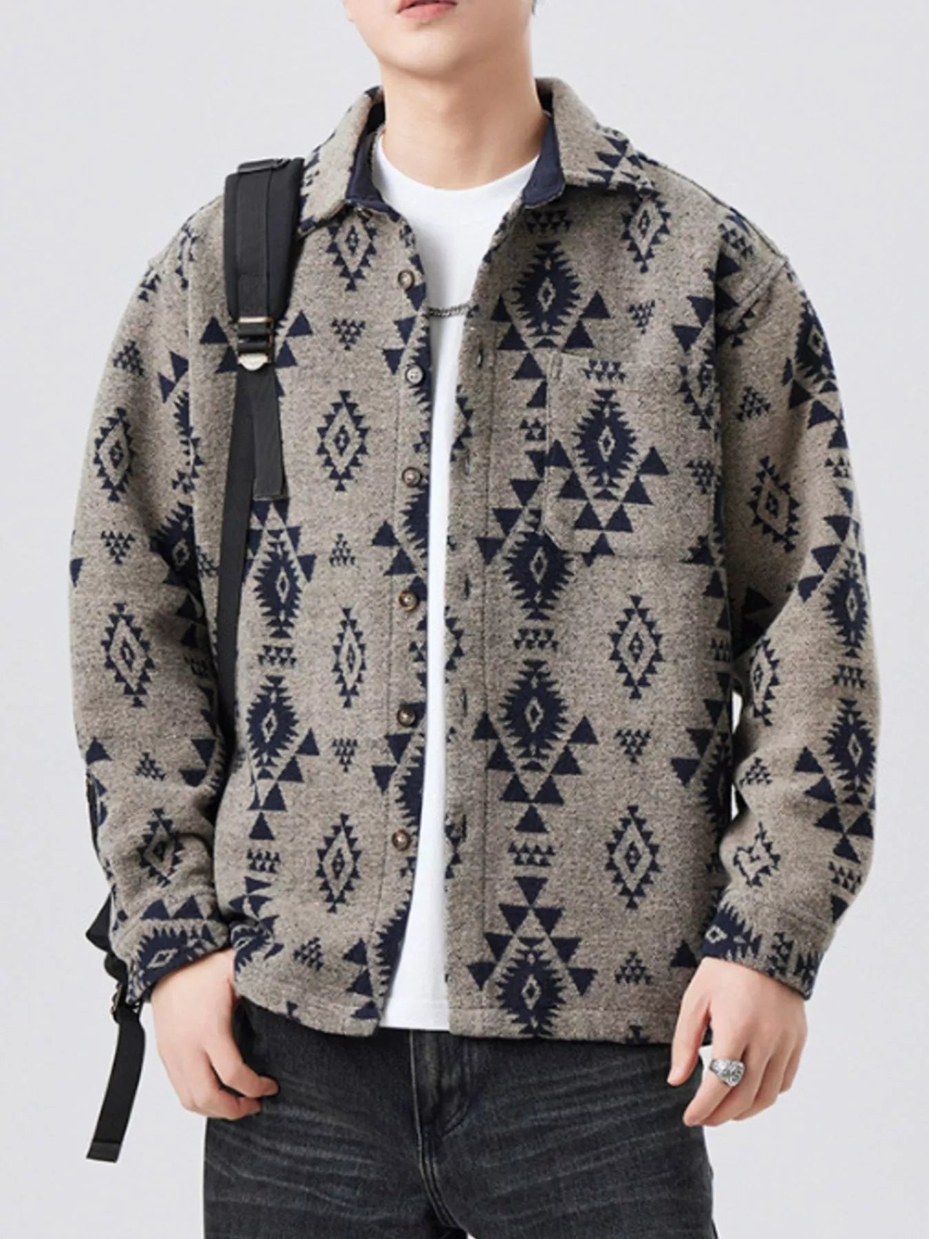 Person wearing a patterned jacket with a white shirt and dark jeans on a light gray background