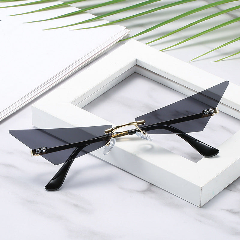 Sunglasses with black lenses and gold accents on a white surface with green leaves in the background