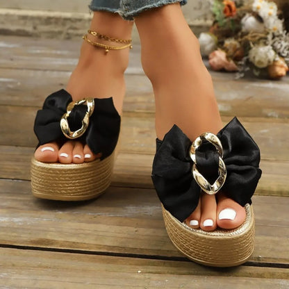 Black sandals with gold rings and large black bows on a wooden floor.