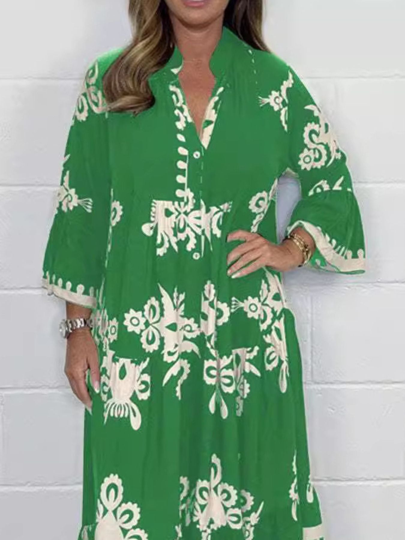 Woman wearing a green dress with white floral patterns against a white brick wall.