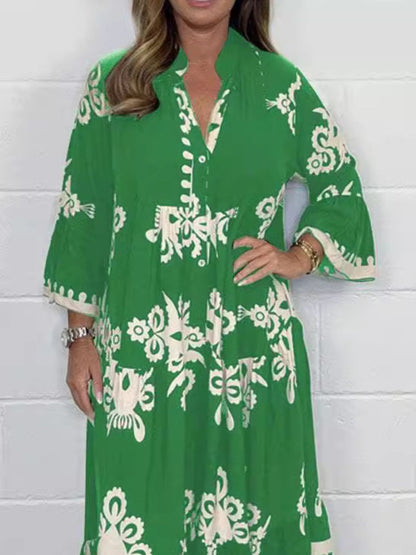Woman wearing a green dress with white floral patterns against a white brick wall.