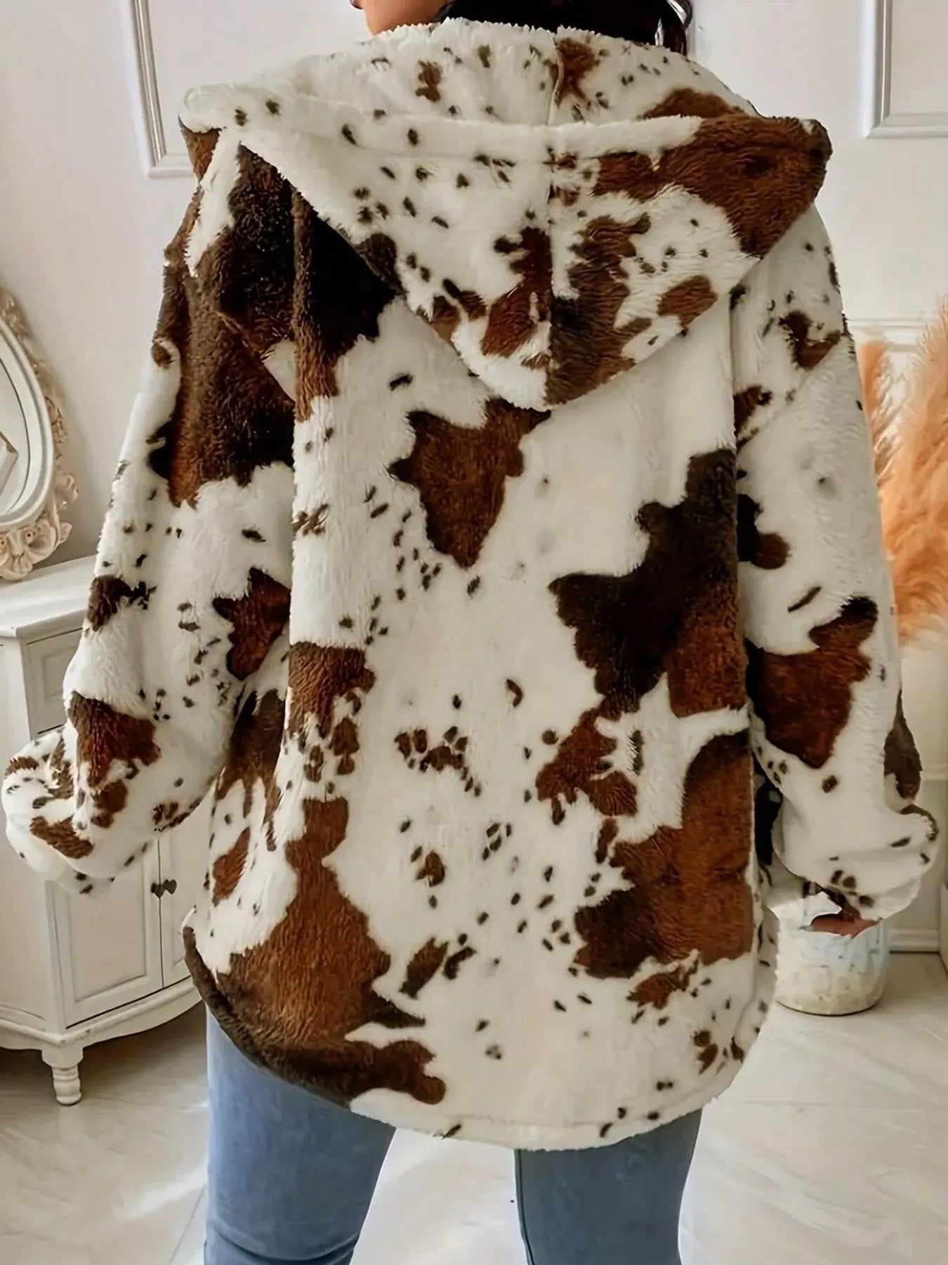 Person wearing a cow print hoodie in a room with a mirror and decorative items.