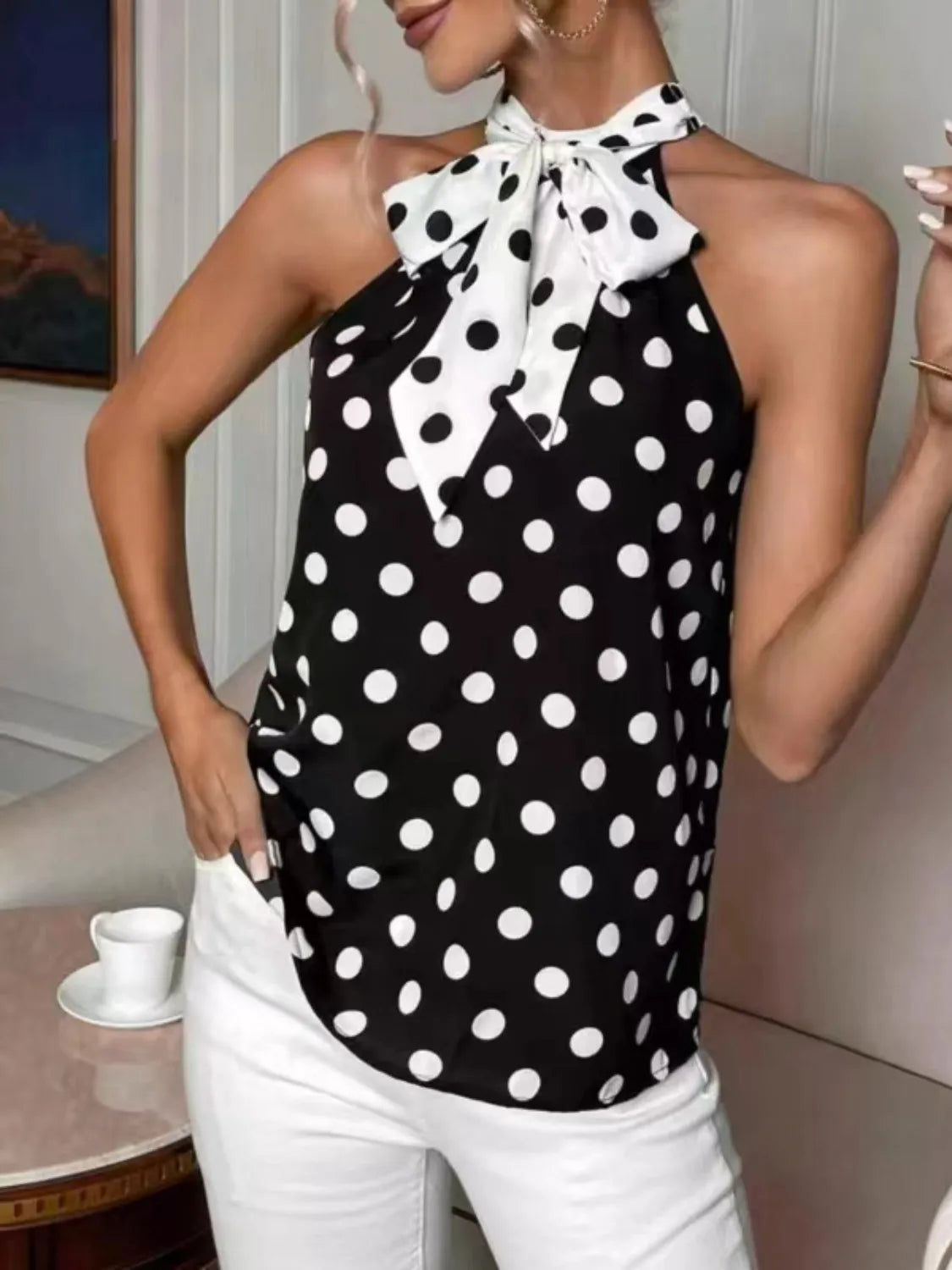 Woman wearing a black and white polka dot halter top with a bow tie in an indoor setting.