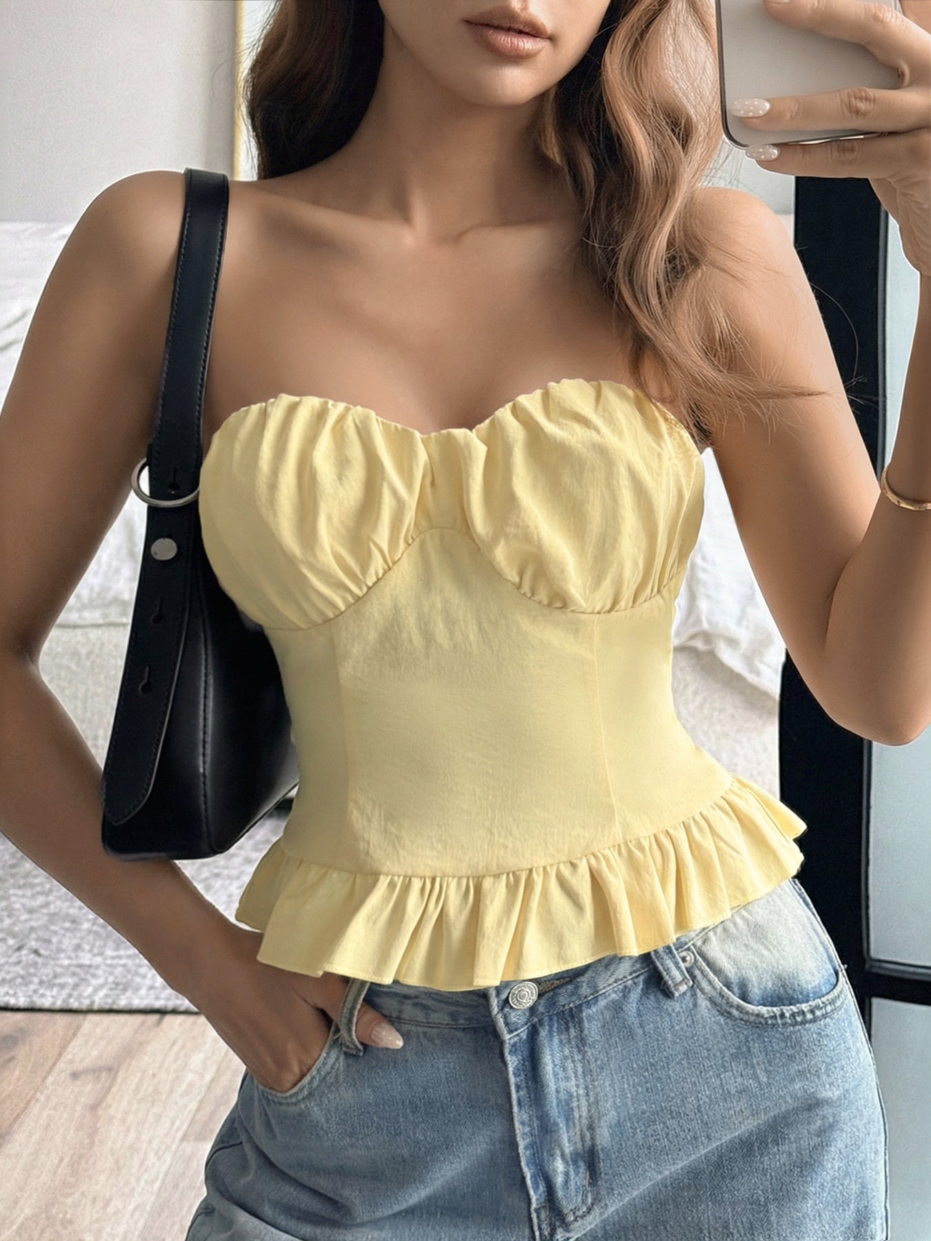 Woman wearing a yellow top and blue jeans, holding a phone.