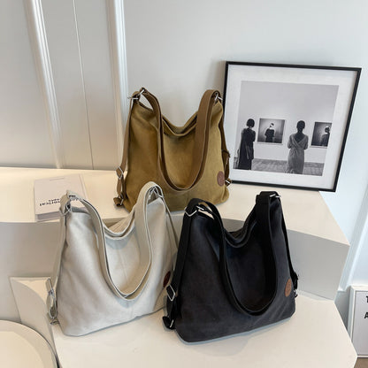 Three handbags in gray, black, and brown on a white surface with a framed picture in the background.