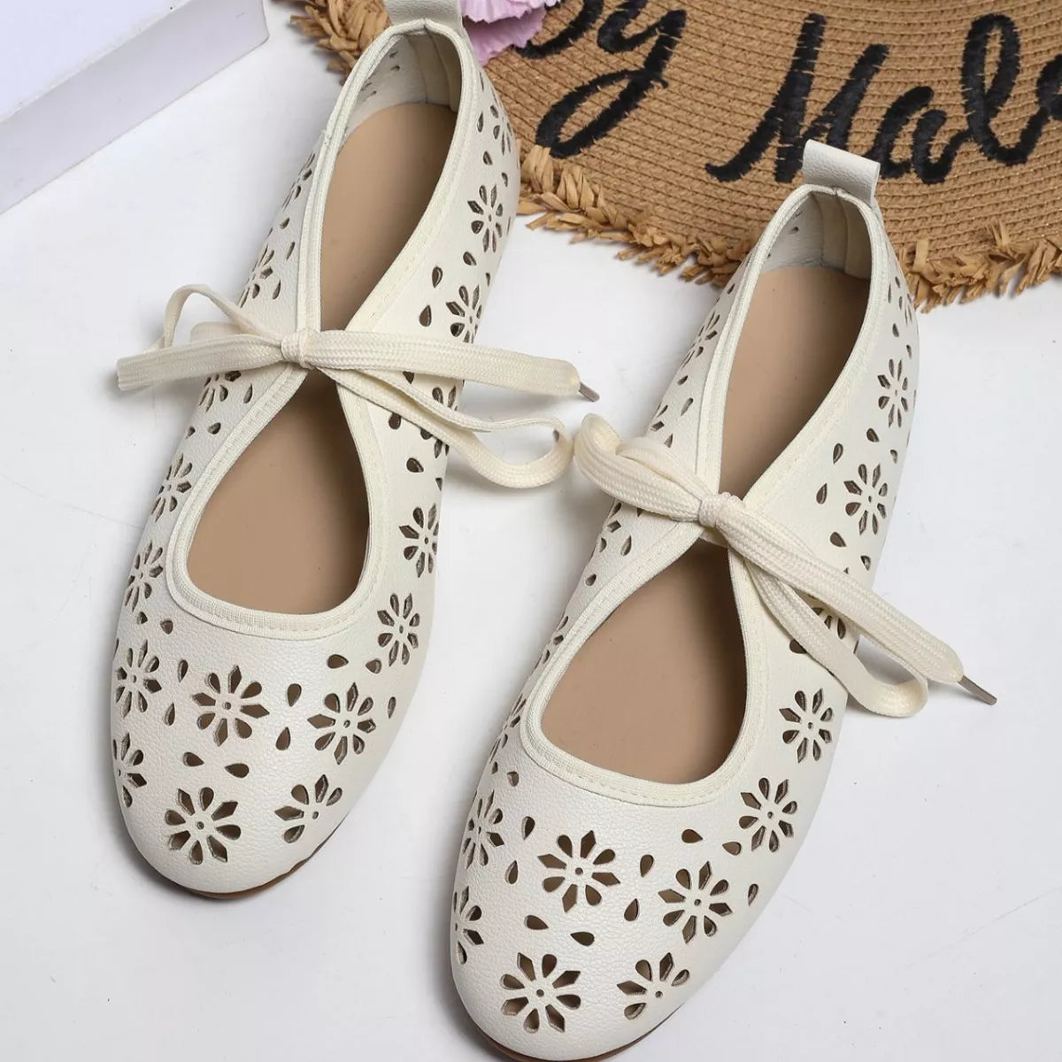 Pair of white ballet flats with floral cutouts on a stone surface