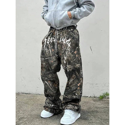 Person wearing camouflage sweat pants against a plain white wall.
