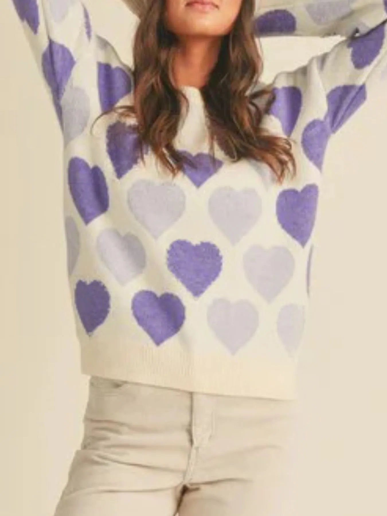 Person wearing a sweater with purple hearts on a beige background