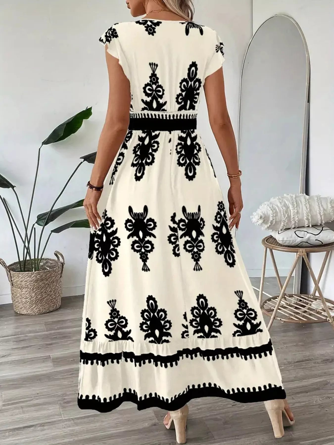 Woman wearing a white dress with black floral patterns in a room.