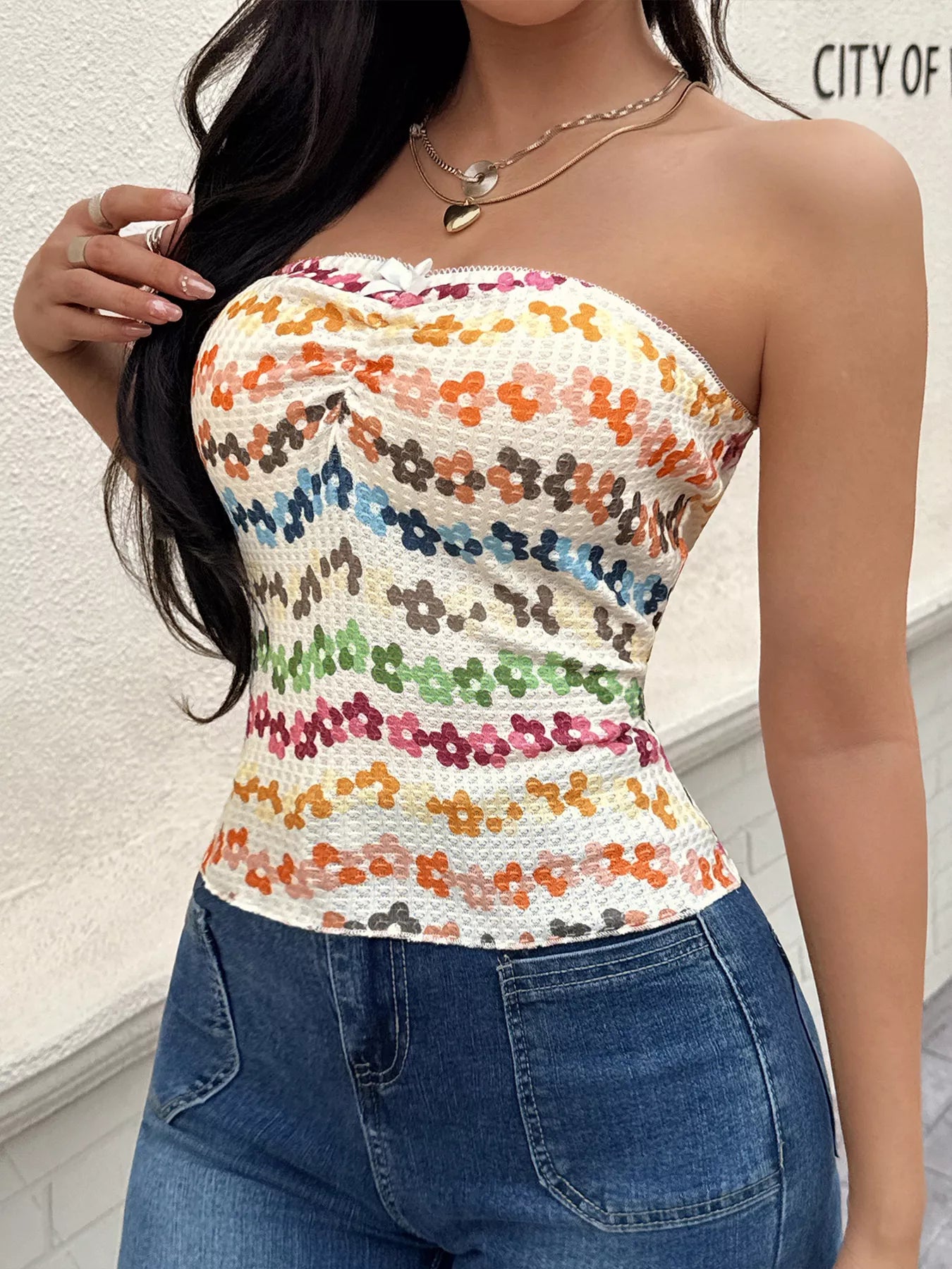 Woman wearing a colorful floral strapless top and blue jeans against a light background.