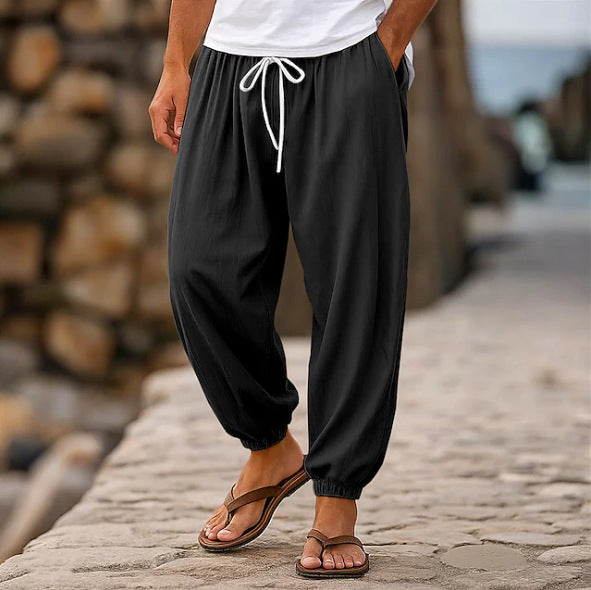 Person wearing black pants with a drawstring, white shirt, and brown sandals on a stone path.