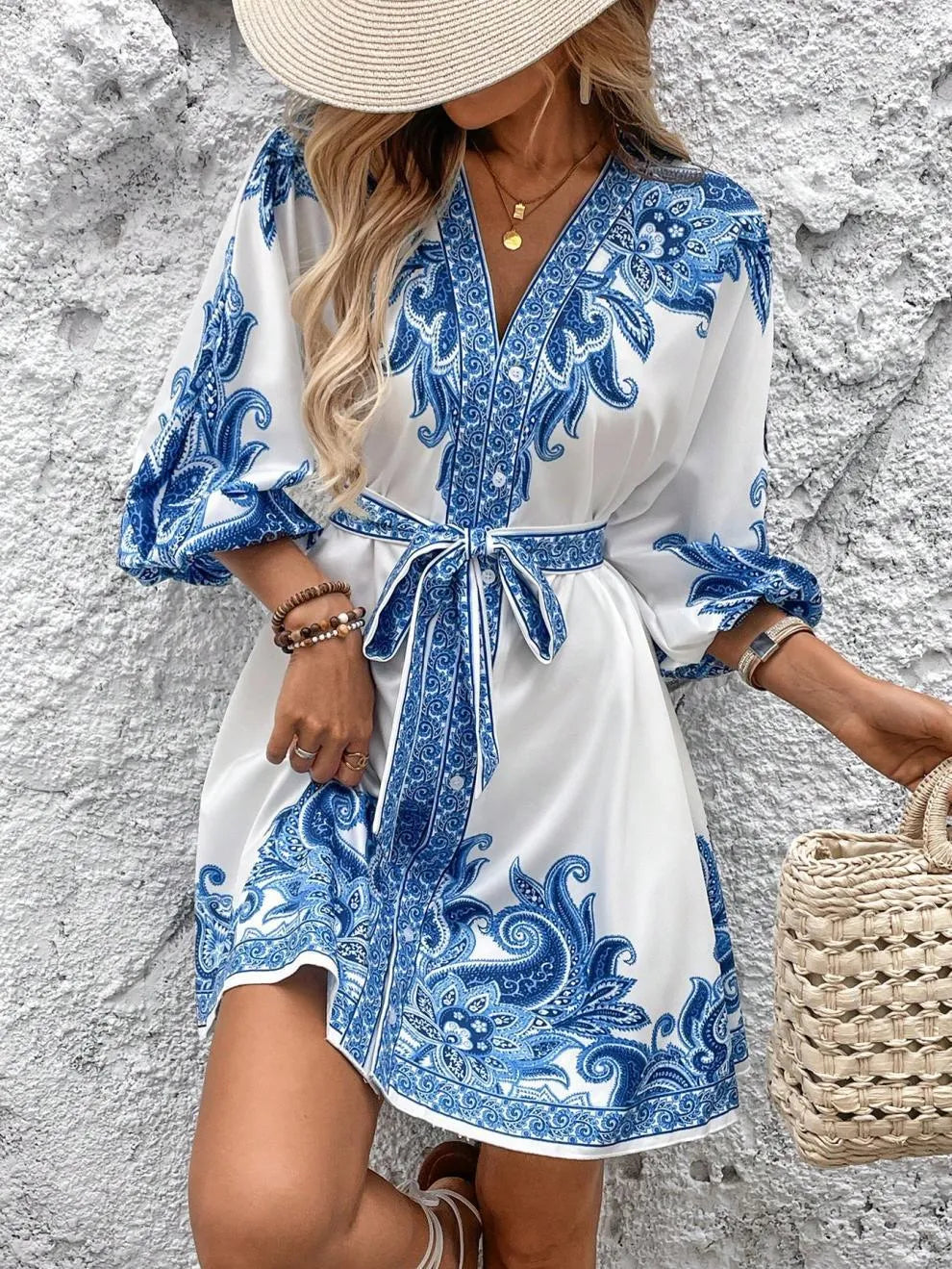 Woman wearing a white dress with blue floral patterns against a textured wall.