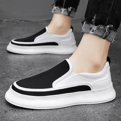 White and black slip-on sneakers worn on a gray pavement.