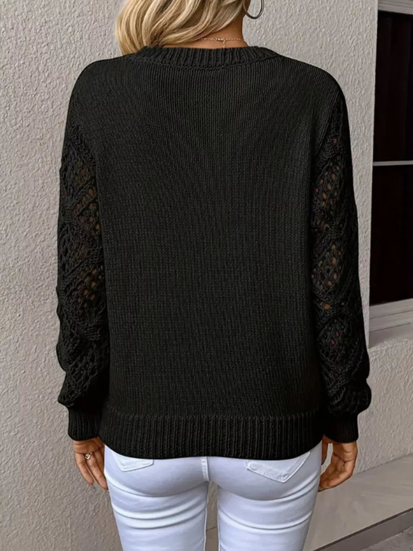 Black sweater with lace sleeves worn by a person against a neutral wall.