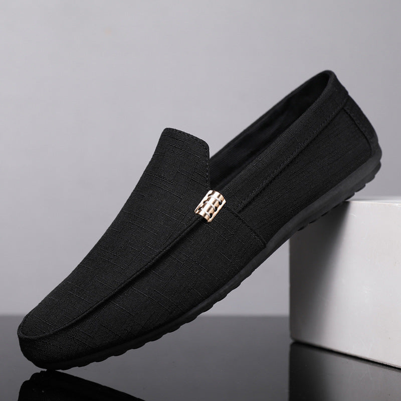 Black loafers with a gold buckle on a gray background
