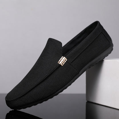 Black loafers with a gold buckle on a gray background