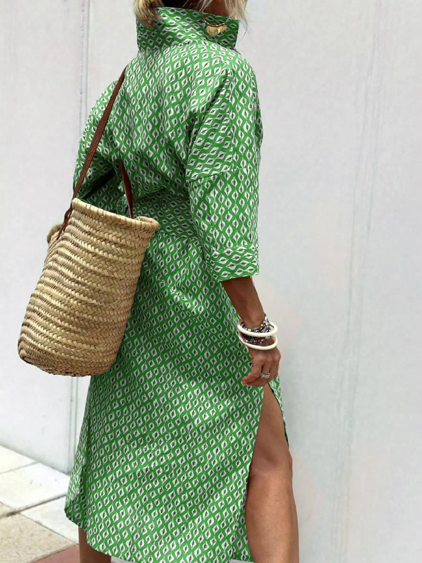 Person wearing a green patterned dress holding a straw bag against a white background