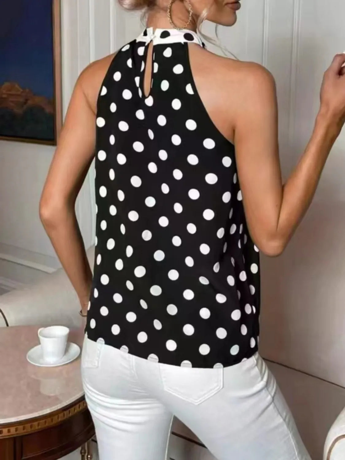 Person wearing a black polka dot halter top and white pants in an indoor setting.