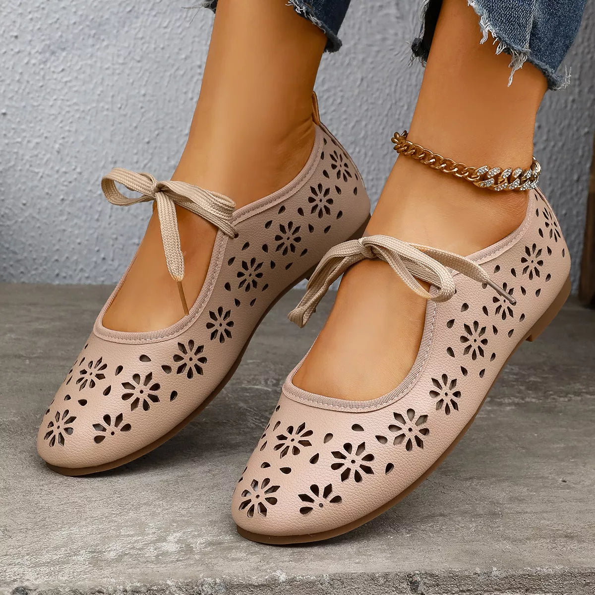 Beige perforated shoes with lace-up design worn by a person on a stone surface.