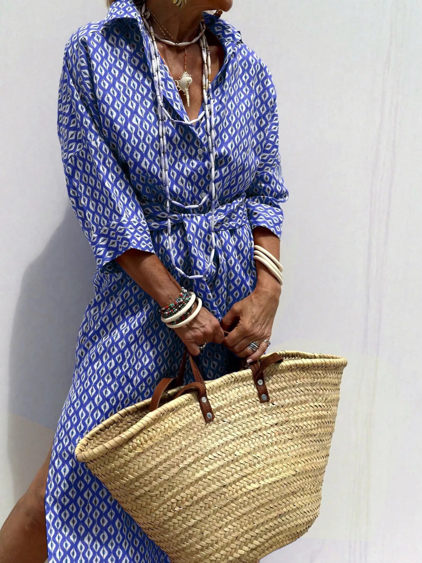 Person wearing a blue patterned dress holding a straw bag against a white background